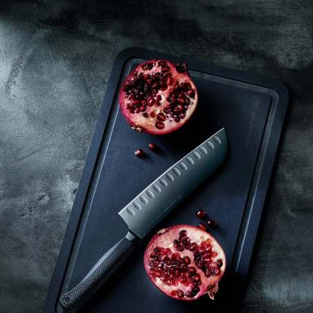 Santoku met kuiltjes Wüsthof Performer naast een opengesneden granaatappel op een donkere snijplank